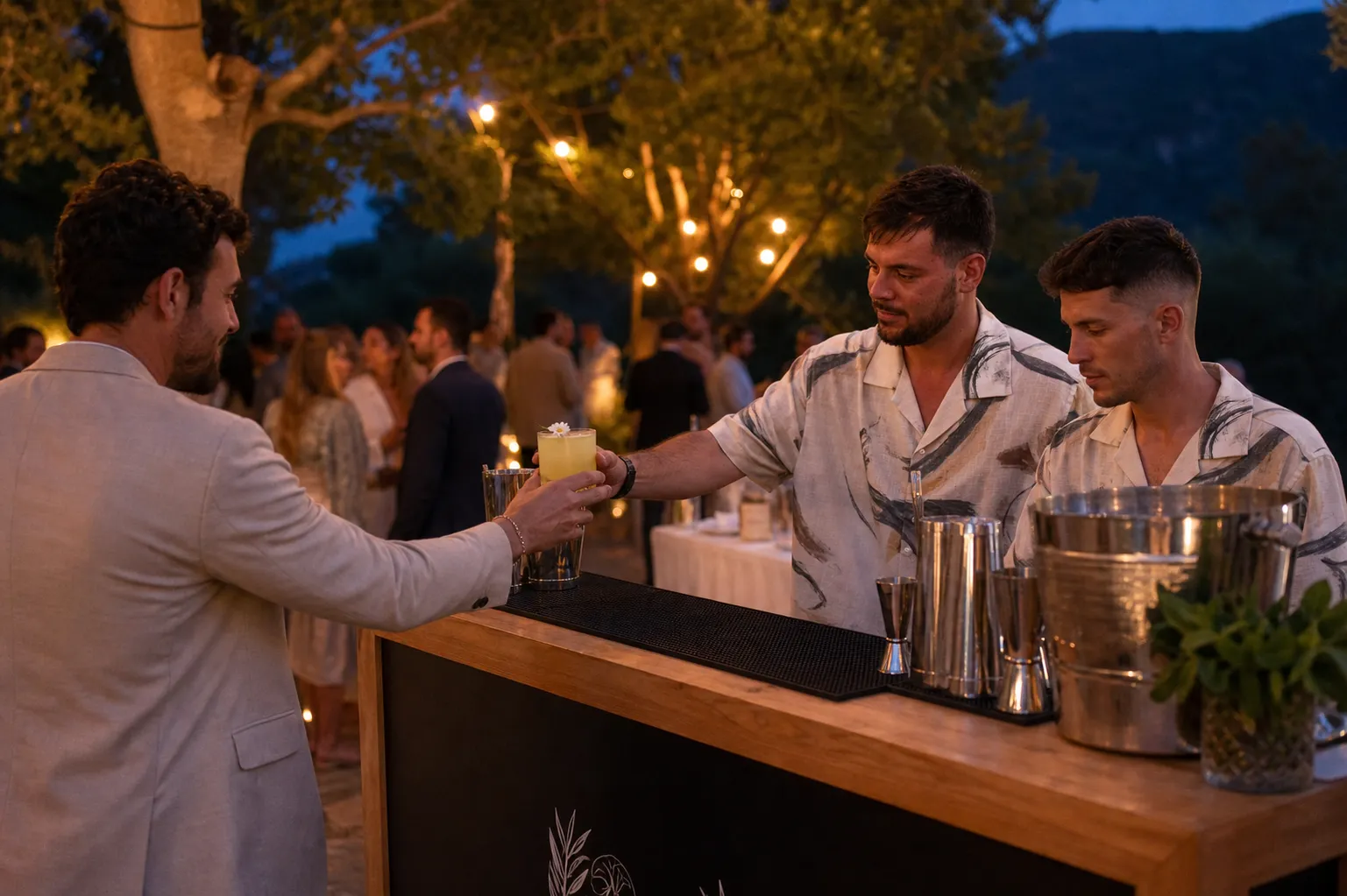 Dos bartenders de Kibou sirviendo en una boda al anochecer, bajo guirnaldas de luces